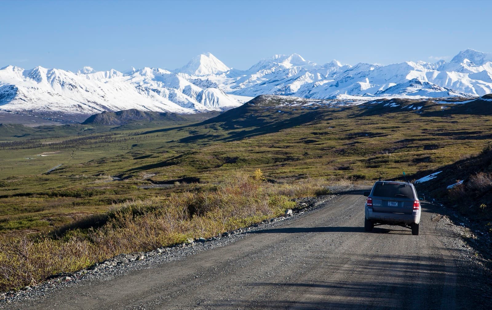 A vehicle on the unpaved Denali Highway heading toward Mount Hayes and the Alaska Range